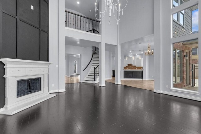 13811 Sugar Dock Ct, Houston, TX 77044 - unfurnished living room featuring a chandelier, a towering ceiling, a fireplace with raised hearth, stairway, and wood finished floors