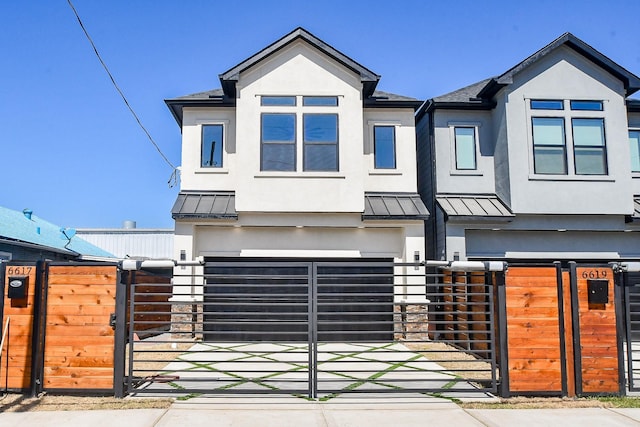 view of front of house featuring a gate, an attached garage, a standing seam roof, and stucco siding