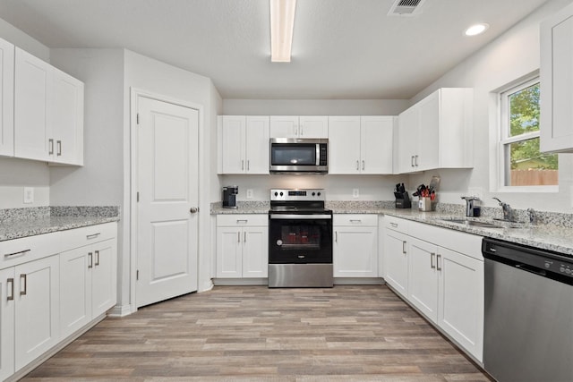 kitchen with appliances with stainless steel finishes, a sink, white cabinetry, and light wood-style flooring