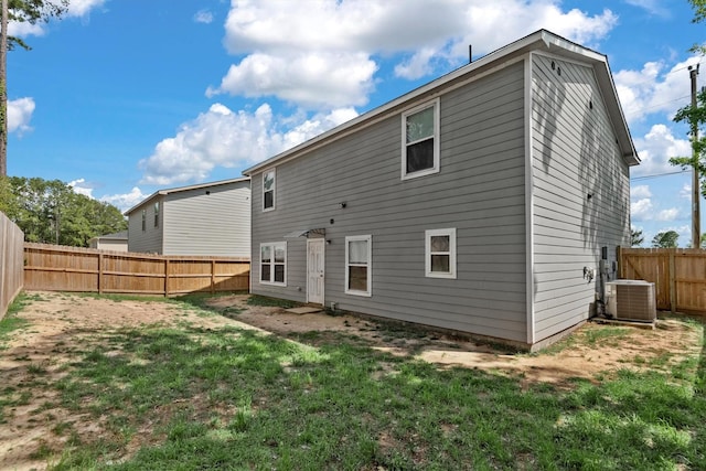 rear view of house with a fenced backyard, a yard, and central AC unit