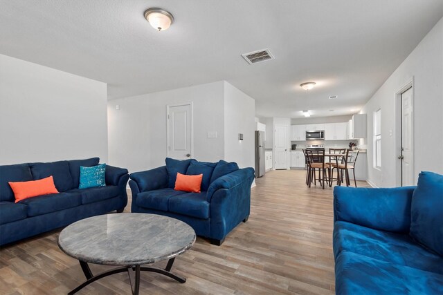 living area with baseboards, visible vents, and light wood-style floors
