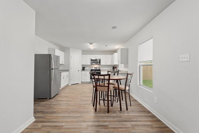 dining area featuring light wood-style floors, visible vents, and baseboards