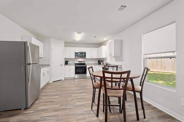 dining space with light wood-type flooring, visible vents, and baseboards