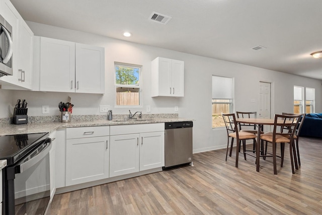 kitchen featuring a sink, appliances with stainless steel finishes, light wood finished floors, white cabinetry, and visible vents