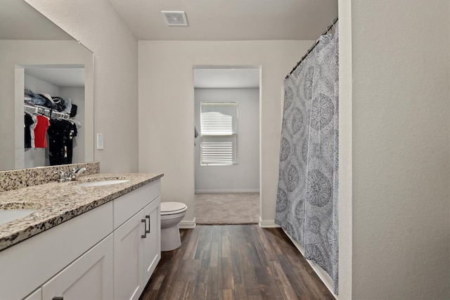 full bath featuring wood finished floors, a sink, double vanity, toilet, and visible vents