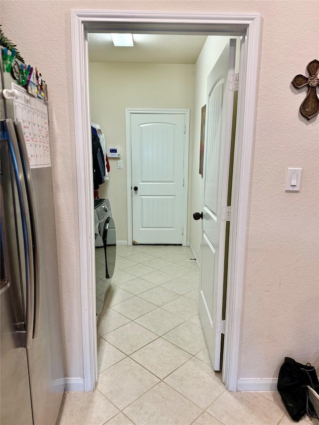 hall featuring washing machine and dryer, baseboards, a textured wall, and light tile patterned floors