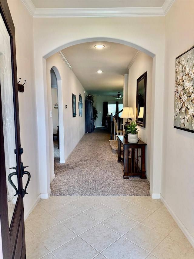 hallway with arched walkways, baseboards, light colored carpet, crown molding, and light tile patterned floors