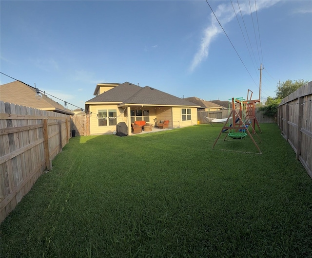 rear view of house with a yard, a fenced backyard, and a playground
