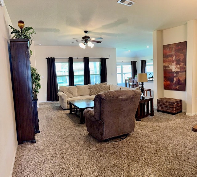 living room featuring baseboards, visible vents, a ceiling fan, and light colored carpet