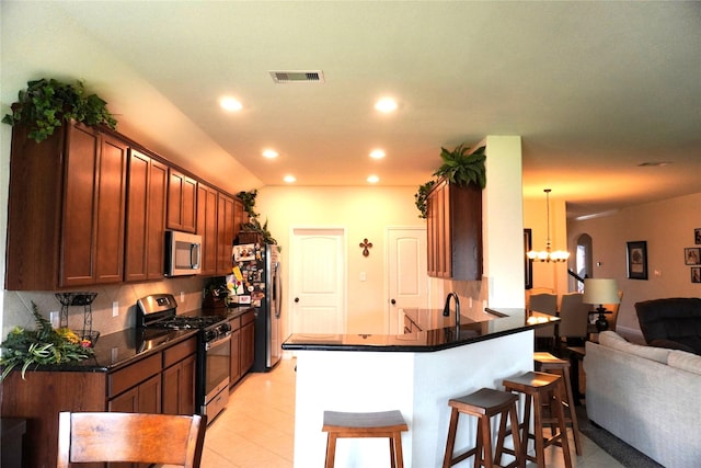 kitchen with dark countertops, a kitchen breakfast bar, stainless steel appliances, a peninsula, and visible vents