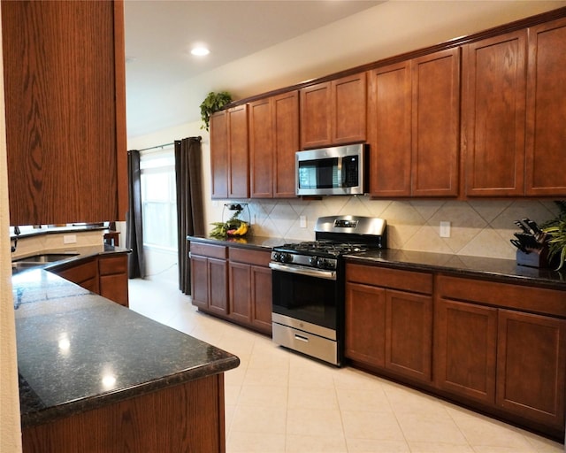 kitchen featuring decorative backsplash, dark stone countertops, stainless steel appliances, and a sink