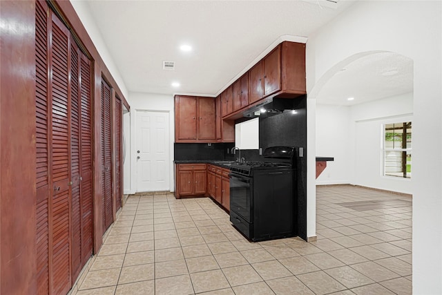 kitchen with under cabinet range hood, visible vents, light tile patterned floors, arched walkways, and black gas stove