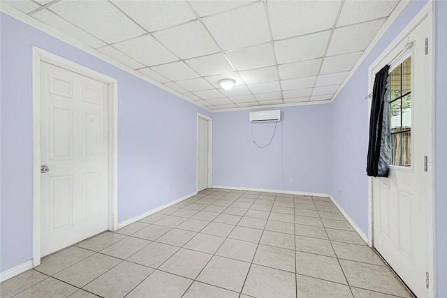 interior space with a wall mounted air conditioner, baseboards, a paneled ceiling, and light tile patterned floors