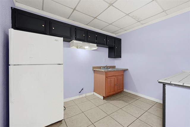 kitchen with a drop ceiling, light tile patterned floors, baseboards, dark cabinets, and freestanding refrigerator