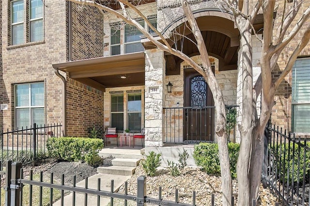 view of exterior entry with a porch, fence, brick siding, and stone siding