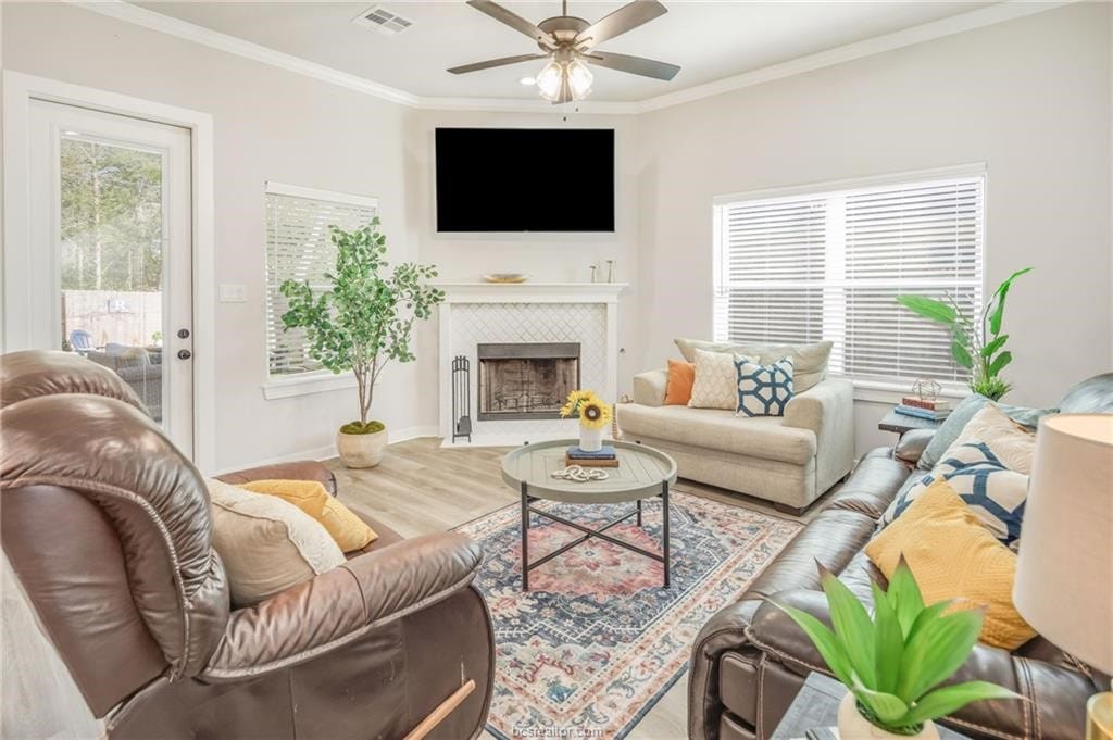 1606 Briscoe Manor Ct, College Station, TX 77845 - living area with wood finished floors, ceiling fan, a tiled fireplace, ornamental molding, and visible vents