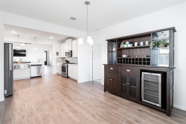 bar featuring stainless steel appliances, wine cooler, visible vents, a sink, and light wood-style flooring