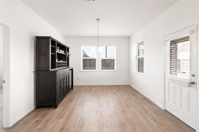 unfurnished dining area featuring a chandelier, light wood-type flooring, and baseboards