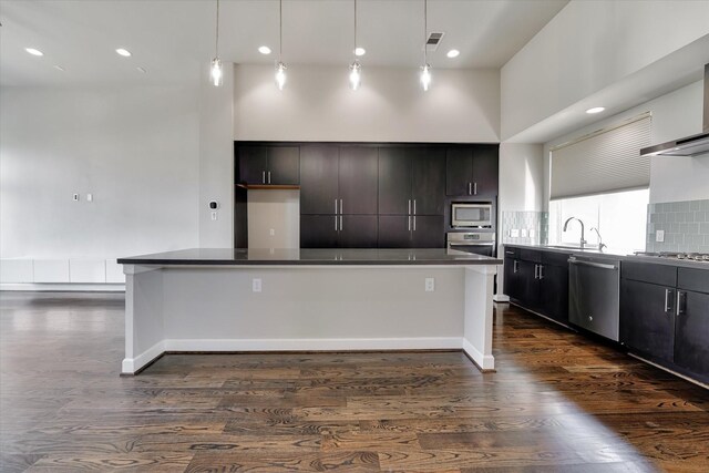 kitchen with dark countertops, a sink, dark wood-type flooring, decorative backsplash, and appliances with stainless steel finishes