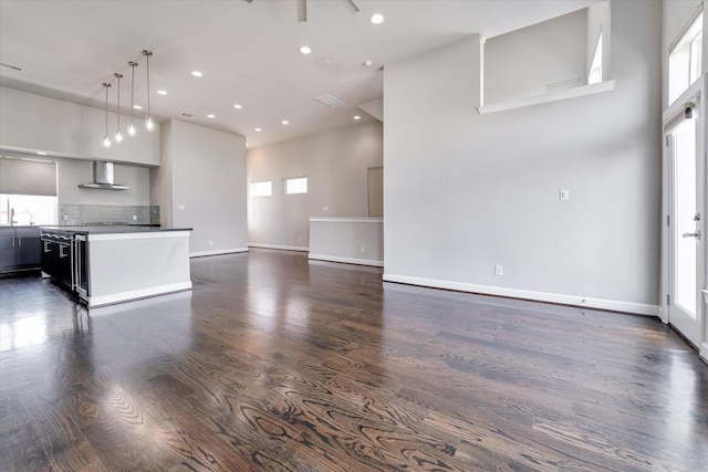 unfurnished living room with recessed lighting, a high ceiling, dark wood-style floors, baseboards, and ceiling fan