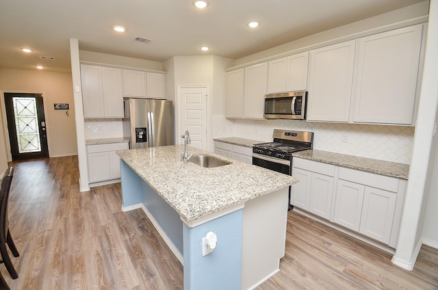 kitchen featuring a sink, stainless steel appliances, backsplash, visible vents, and a center island with sink