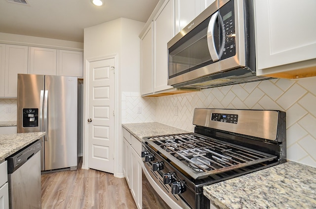 kitchen featuring appliances with stainless steel finishes, tasteful backsplash, light stone counters, white cabinets, and light wood-style flooring