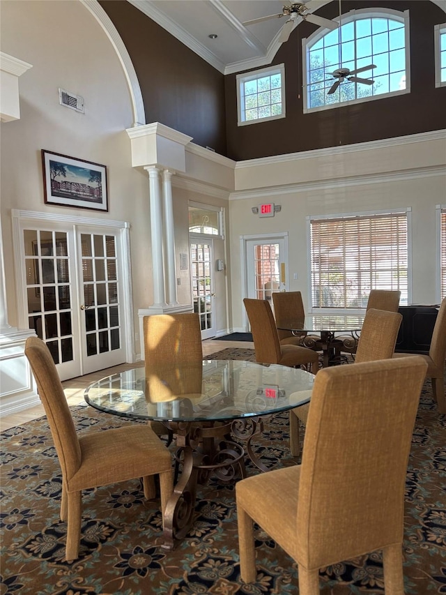 dining room featuring crown molding, a ceiling fan, a towering ceiling, ornate columns, and visible vents