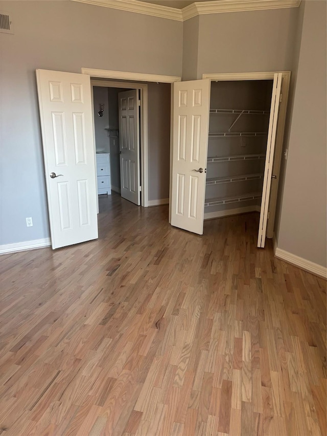 unfurnished bedroom featuring a walk in closet, crown molding, baseboards, a closet, and light wood finished floors