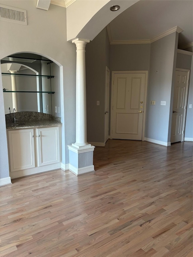 interior space featuring crown molding, light wood finished floors, arched walkways, decorative columns, and visible vents