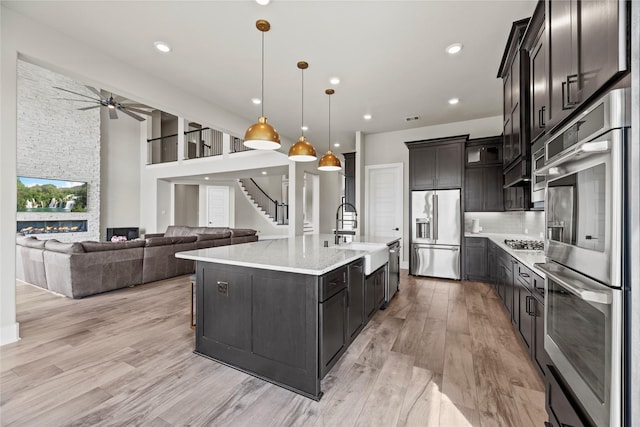 kitchen with stainless steel appliances, light wood-style flooring, a sink, backsplash, and ceiling fan