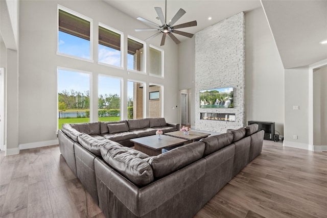 living room featuring light wood-style flooring, a high ceiling, baseboards, and ceiling fan