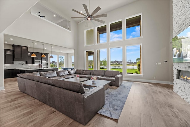 living area featuring a fireplace, light wood-style floors, plenty of natural light, and a high ceiling
