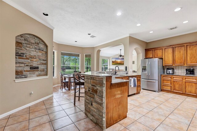 kitchen featuring brown cabinets, light tile patterned flooring, appliances with stainless steel finishes, ornamental molding, and visible vents