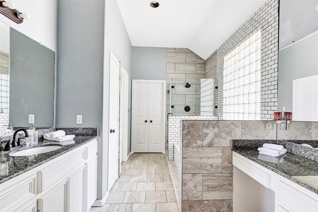full bath with vaulted ceiling, a sink, a stall shower, baseboards, and two vanities