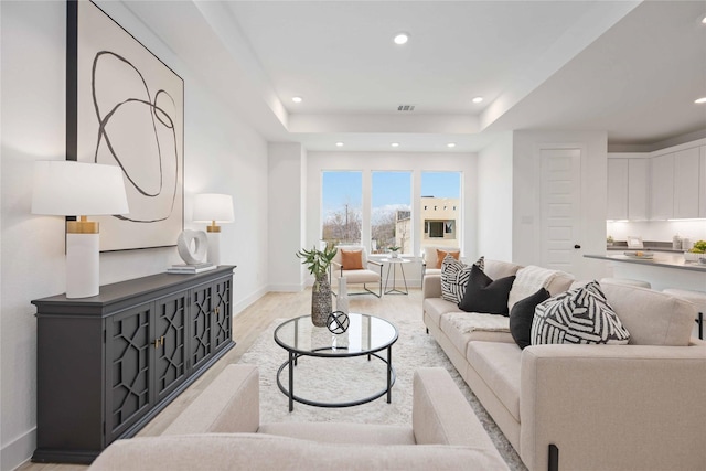 living room featuring recessed lighting, light wood-style flooring, baseboards, and a tray ceiling