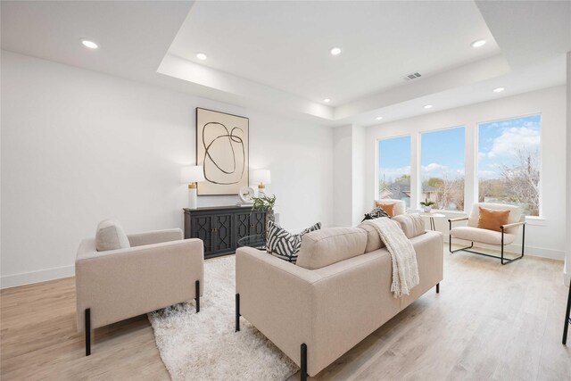 living room with light wood finished floors, a tray ceiling, visible vents, and recessed lighting