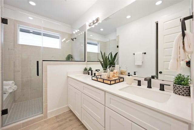 full bathroom featuring wood finished floors, a sink, double vanity, and a stall shower