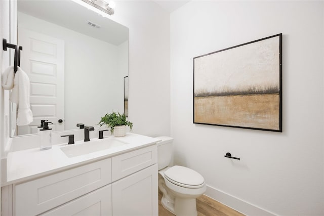 bathroom with wood finished floors, vanity, baseboards, toilet, and visible vents