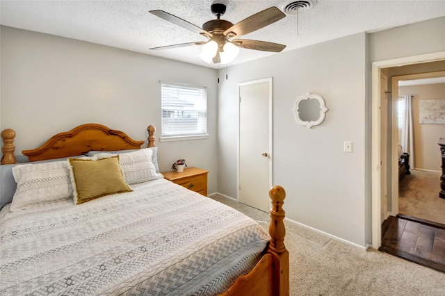 bedroom featuring carpet flooring, a textured ceiling, visible vents, baseboards, and ceiling fan