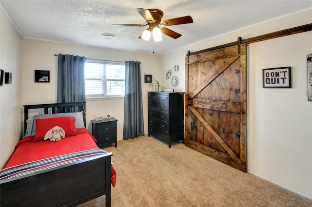 bedroom featuring a barn door, carpet floors, a textured ceiling, and a ceiling fan