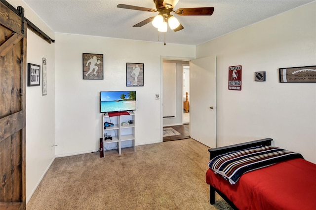 bedroom featuring a textured ceiling, a barn door, baseboards, carpet, and ceiling fan