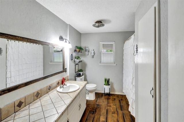 bathroom with wood finished floors, a textured wall, toilet, vanity, and a textured ceiling