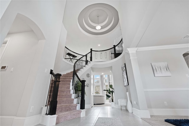 tiled entryway with stairway, arched walkways, baseboards, and a towering ceiling