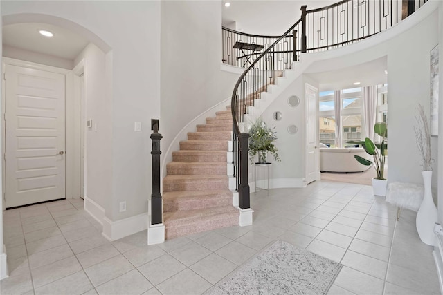 foyer entrance featuring baseboards, arched walkways, tile patterned floors, and stairway