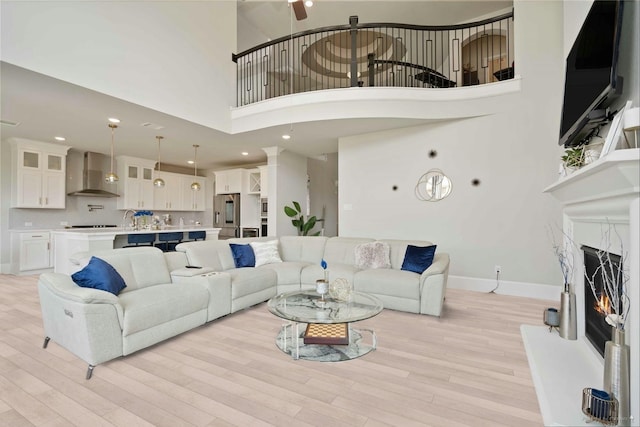 living room with a warm lit fireplace, a high ceiling, baseboards, and light wood-type flooring