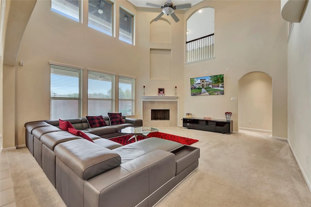 living area featuring ceiling fan, arched walkways, carpet floors, a fireplace, and a high ceiling