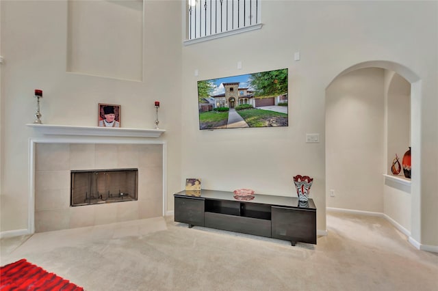 carpeted living area featuring arched walkways, a tiled fireplace, a high ceiling, and baseboards
