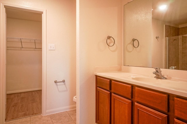 bathroom with a spacious closet, vanity, baseboards, tile patterned floors, and tiled shower
