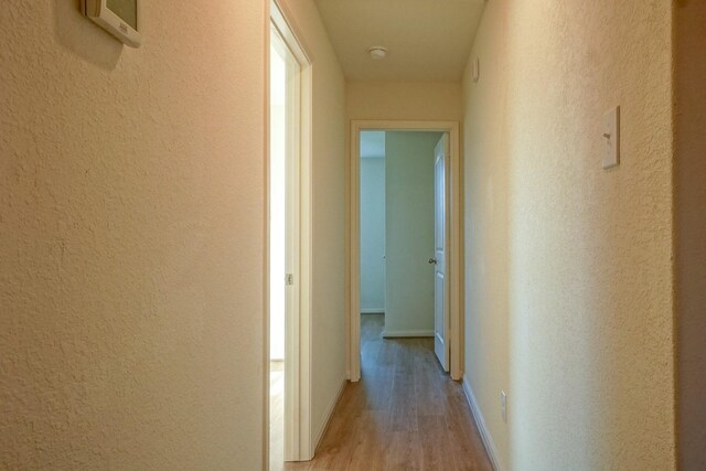 hall with light wood-type flooring, a textured wall, and baseboards