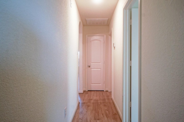 hallway featuring light wood-style floors, baseboards, and a textured wall